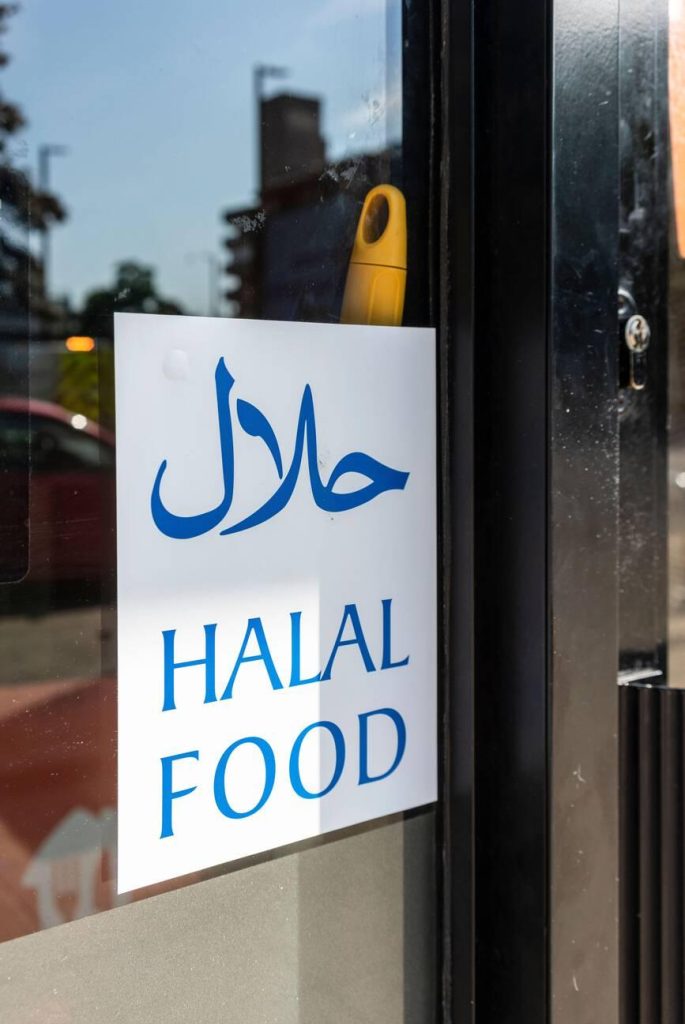 A'Halal Food' sign with both Arabic (حلال) and English text, displayed on the glass door of a restaurant to indicate that it offers halal certified products.