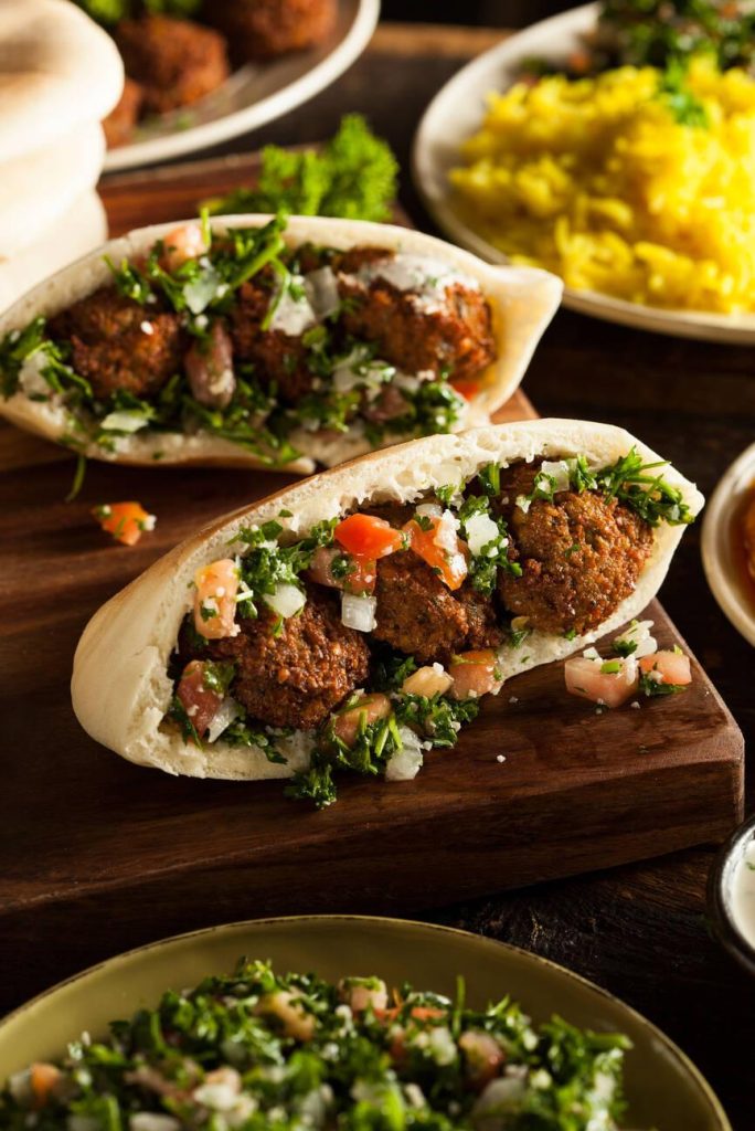 Two falafel sandwiches in pita bread, filled with fresh parsley and chopped vegetables, served on a wooden board