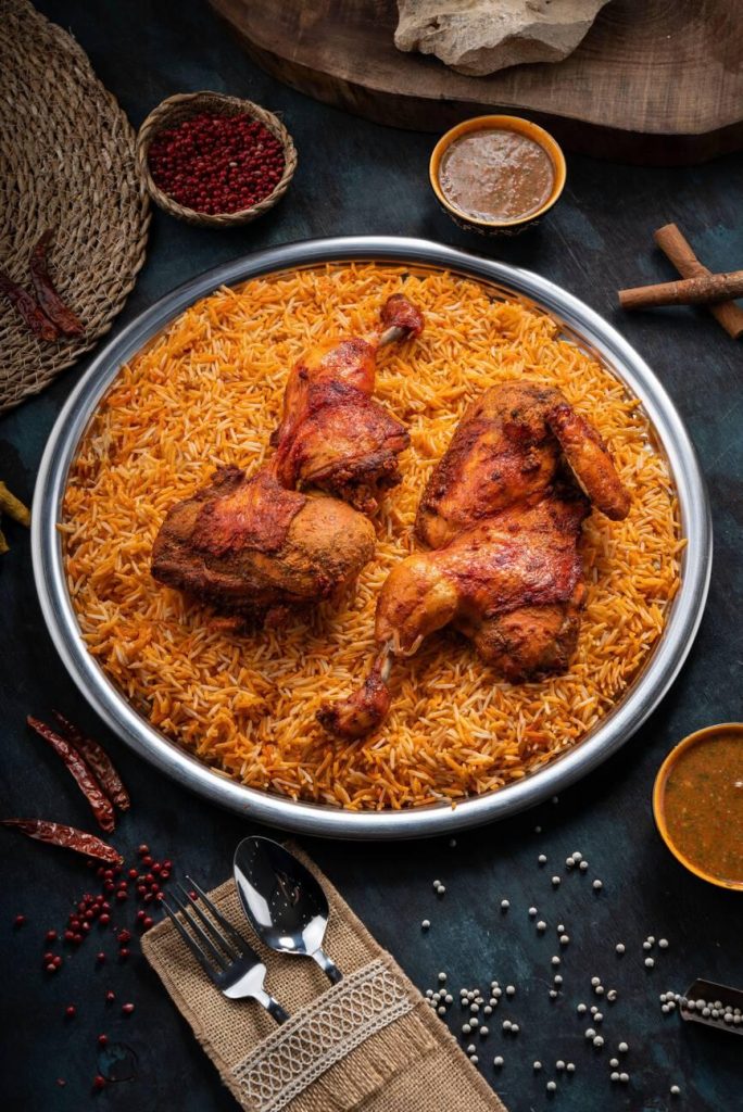 Mandi rice dish with grilled chicken meat and spices on a dark green background