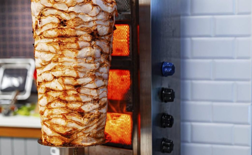 A large rotating spit of chicken Shawarma cooking on a vertical grill, a popular Halal dish in Middle Eastern cuisine.