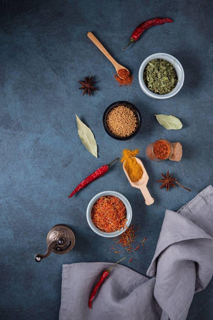 Various bowls and spoons of oriental spices on dark blue background with towel. Top view and flat lay