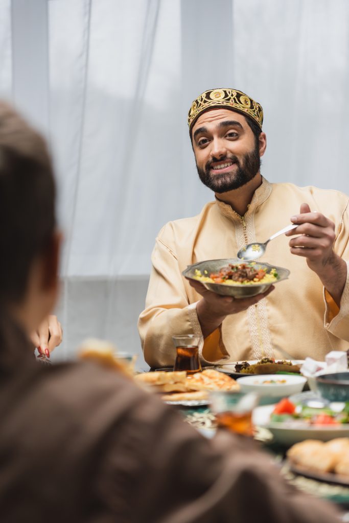 Positive muslim father holding food near blurred family during ramadan at home