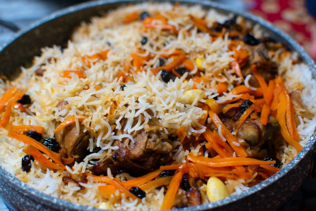 A dish of Halal Afghan Kabuli Pulao, featuring rice mixed with carrots and raisins, served in a traditional metal bowl.