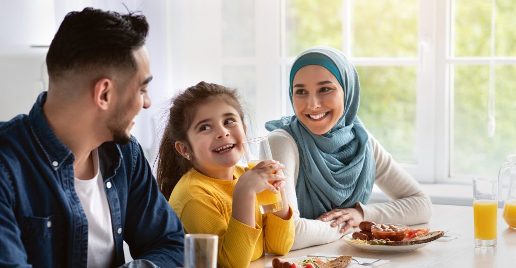 Happy islamic family with little daughter eating tasty breakfast 