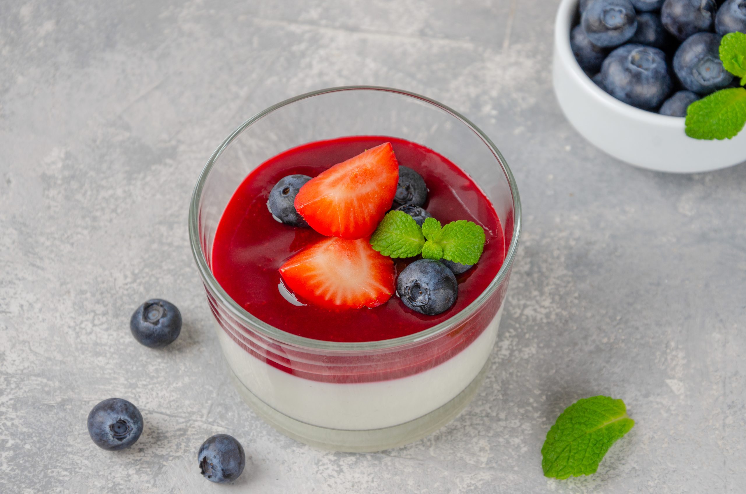 Italian dessert panna cotta in a glass with berry sauce, fresh strawberries and blueberries on top on a gray concrete background. Copy space. Italian dessert panna cotta in a glass with berry sauce, fresh strawberries and blueberries on top on a gray concrete background. Copy space.