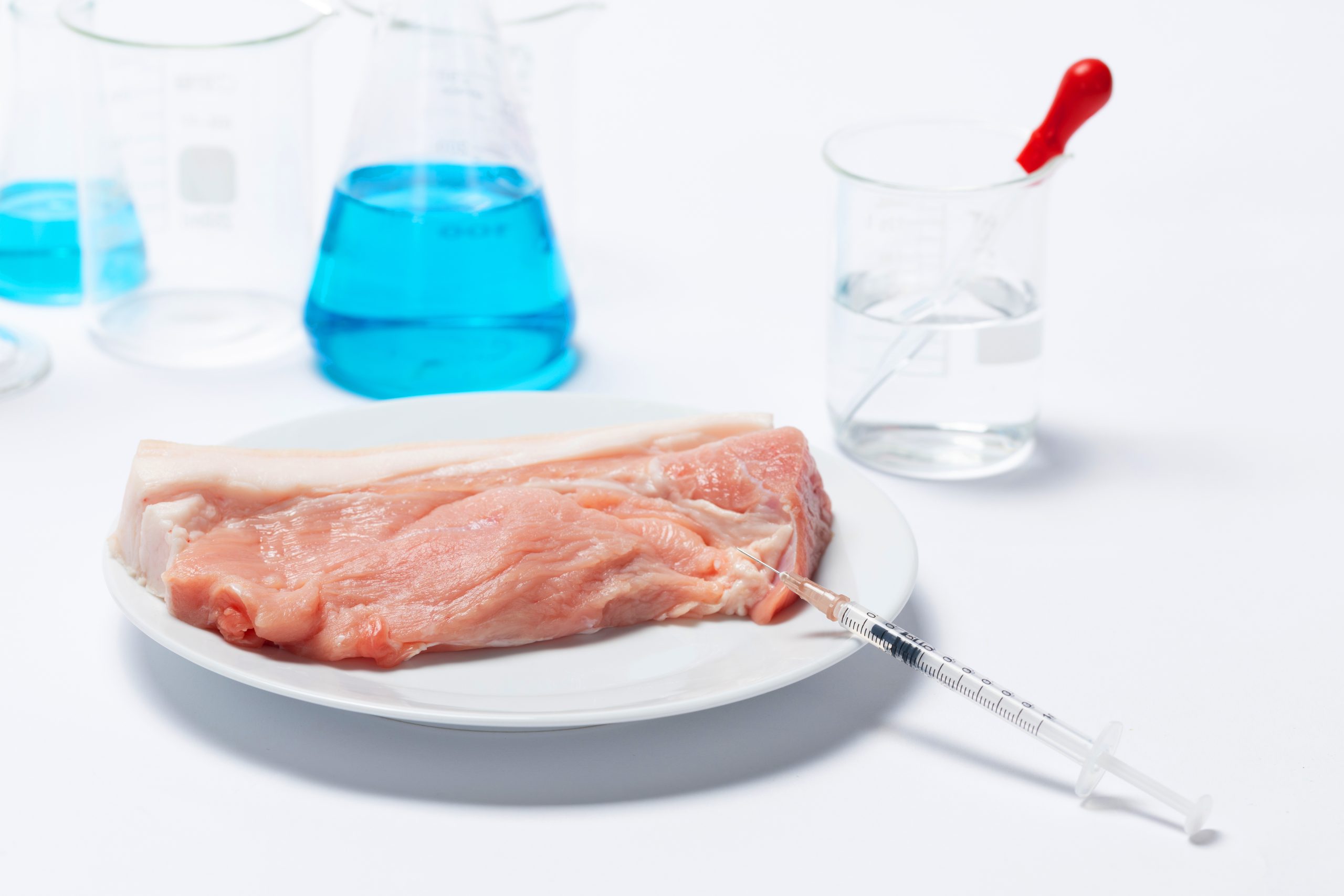Piece of raw meat with oxic substances in glass beakers and a syringe needle on the table
