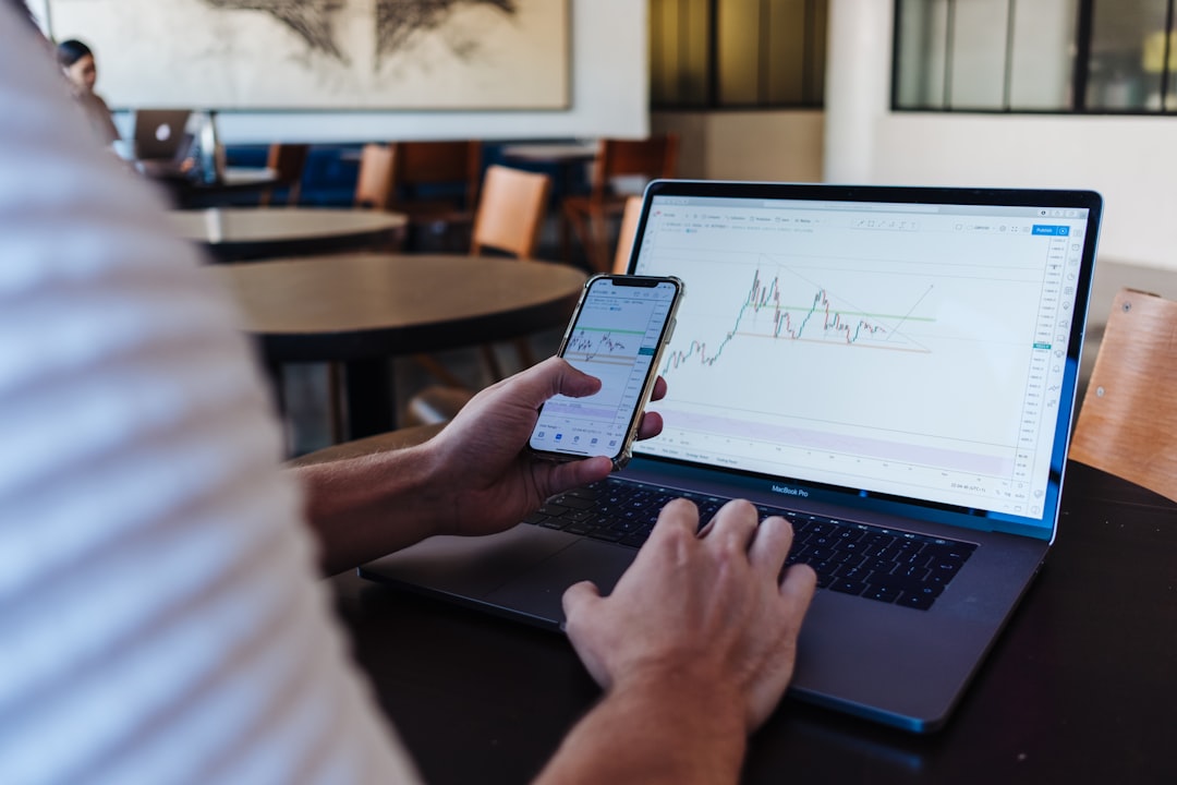 Investor using a smartphone and laptop to review a portfolio