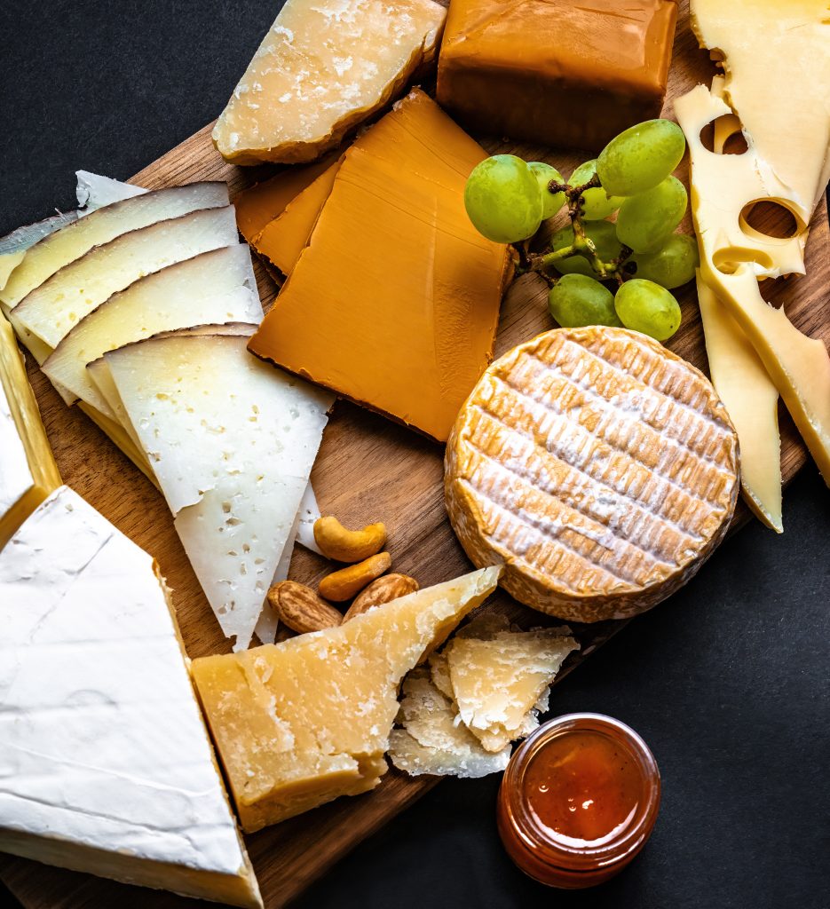 Assorted cheeses with grapes and jam on a wooden board
